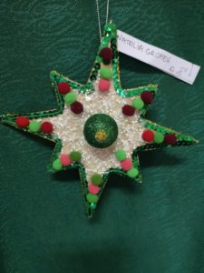 Na zdjęciu: Gwiazdka o dłuższych i krótszych ramionach. Ozdobiona od zewnątrz zielonymiu cekinkami oraz zielonymi i czerwonymi kuleczami. Tło stanowi biała kaszka.