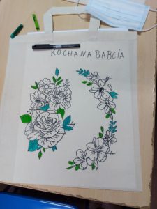 Na zdjęciu: jasna, materiałowa torba ozdobiona kwiatowym wzorem z napisem KOCHANA BABCIA.