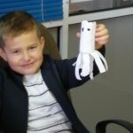 Na zdjęciu: Uśmiechnięty chłopiec pokazuje białego stworka z papieru.