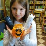 Na zdjęciu: Dziewczynka - trzyma lampion wykonany ze słoika i pomarańczowej bibuły oraz dwa stworki z rolek po papierze toaletowym - biały i czarny.