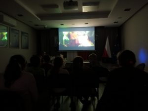 Na zdjęciu: Ciemna sala, ciemne sylwetki osób i jasny ekran z kadremz filmu.
