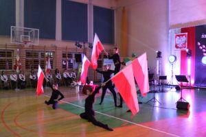 Na zdjęciu: Ubrane na czarno dziewczyny w różnych pozycjach trzymają flagi Polski.