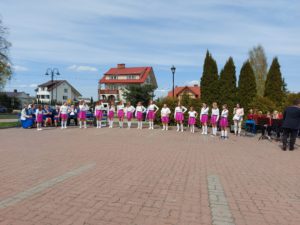 Na zdjęciu: Dziewczynki w białych bluzkach, różowych spódnicach i białych długich skarpetkach stoją w rzędzie.