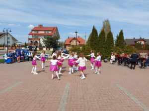 Na zdjęciu: Dziewczynki w białych bluzkach, różowych spódnicach i białych długich skarpetkach tańczą w kółku.
