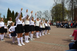 Na zdjęciu: Dziewczynki, ubrane w białe bluzki, czarne spódnice i białe skarpetki stoją w rzędach i mają do góry podniesione ręce.