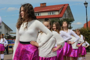 Na zdjęciu: Dziewczynkiw białych bluzkach, różowych spódnicach i białych długich skarpetkach stoją z jedną ręką opartą o biodro.