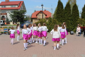 Na zdjęciu: Dziewczynkiw białych bluzkach, różowych spódnicach i białych długich skarpetkachwykonują układ taneczny z jedną ręką opartą o biodro.