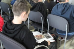 Na zdjęciu: Chłopiec siedzi na krześle i ogląda książkę, którą trzyma na kolanach.