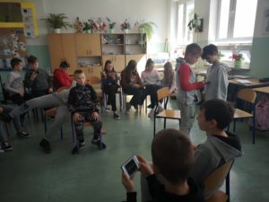 Na zdjęciu: W szkolnej klasie dzieci siedzą na krzesełkach w kole. Wykoują zadanie na telefonach.