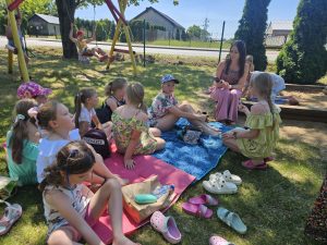 Dzieci siedzą na kocu i słuchają kobiety, która czyta książkę