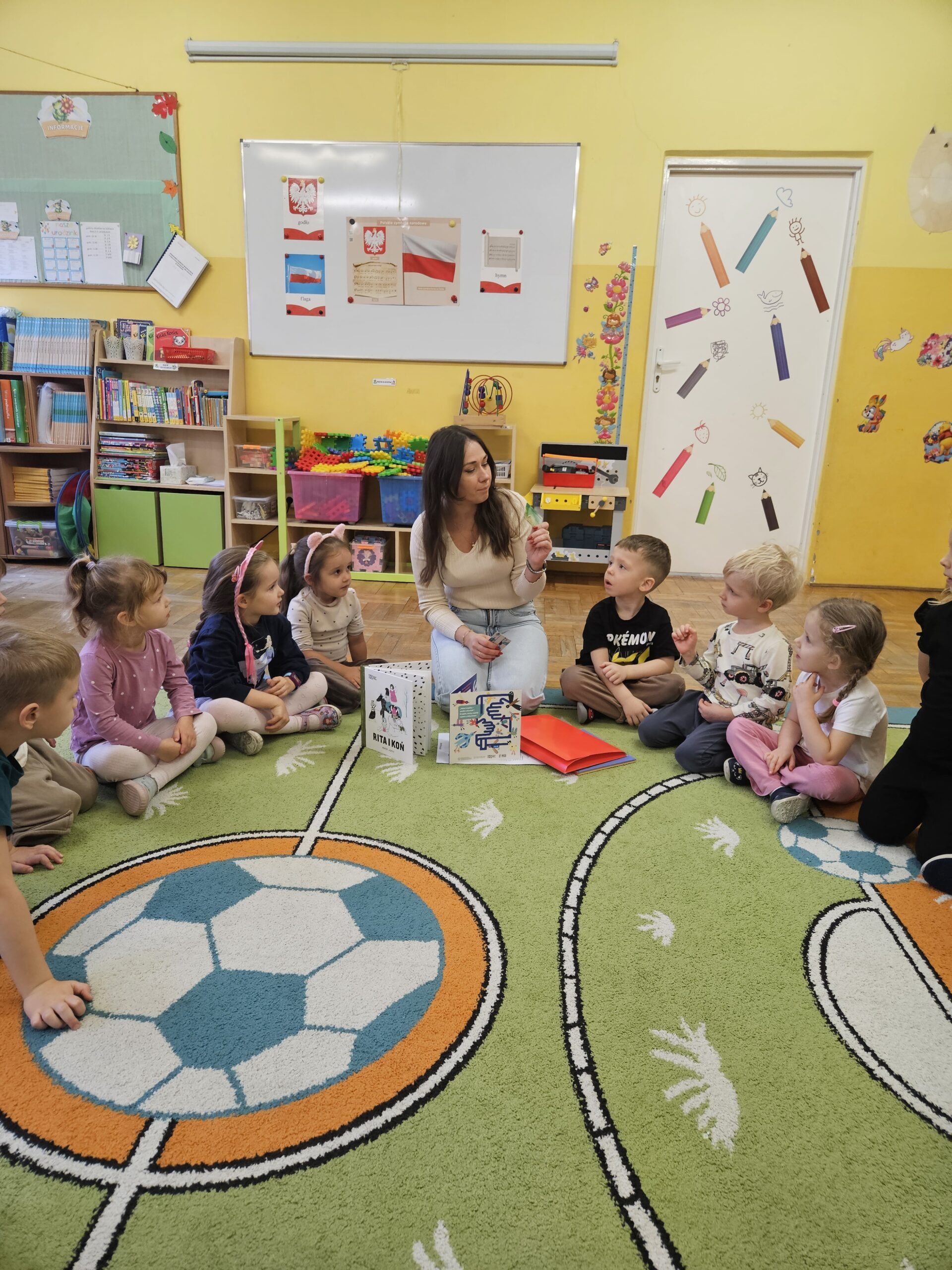 Kobieta oraz dzieci siedzące w kółku, na podłodze