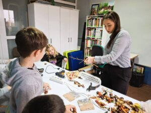 20251113_150047 Dzieci i kobieta, na warsztatach, robiące ptaszki z kasztanów