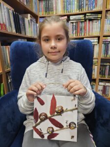 20251113_154626 Dziewczynka trzymająca obrazek z ptaszkami z kasztanów.