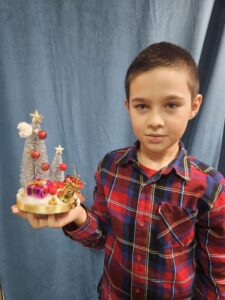 Zdjęcie przedstawia chłopca pokazującego swoją pracę