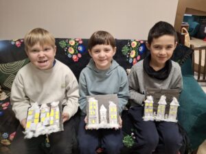 Chłopcy prezentują swoje obrazki z domkami i watą.