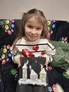 Dziewczynka prezentująca swój obrazek z domkami i watą.