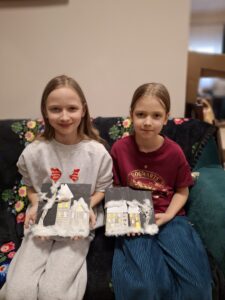 Dziewczynki prezentują swoje obrazki z domkami i watą.