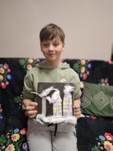 Chłopiec prezentuje swój obrazek z domkami i watą.