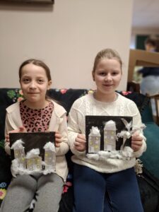 Dziewczynki prezentują swoje obrazki z domkami i watą.