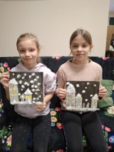 Dziewczynki prezentują swoje obrazki z domkami i watą.