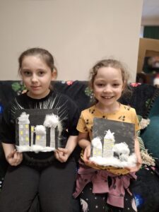 Dziewczynki prezentują swoje obrazki z domkami i watą.