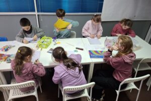 Dzieci na warsztatach tworzą maski karnawałowe.