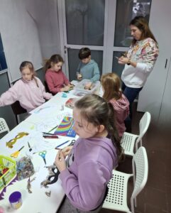 Dzieci na warsztatach tworzą maski karnawałowe.