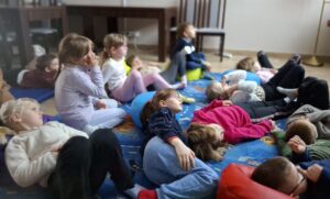 Dzieci leżą na dywanie podczas lekcji bibliotecznej.