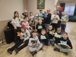 Grupowe zdjęcie dzieci trzymających w rękach przyborniki z papieru w kształcie kota oraz ich nauczycielka.
