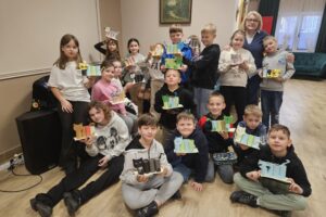 Grupowe zdjęcie dzieci trzymających w rękach przyborniki z papieru w kształcie kota oraz ich nauczycielka.