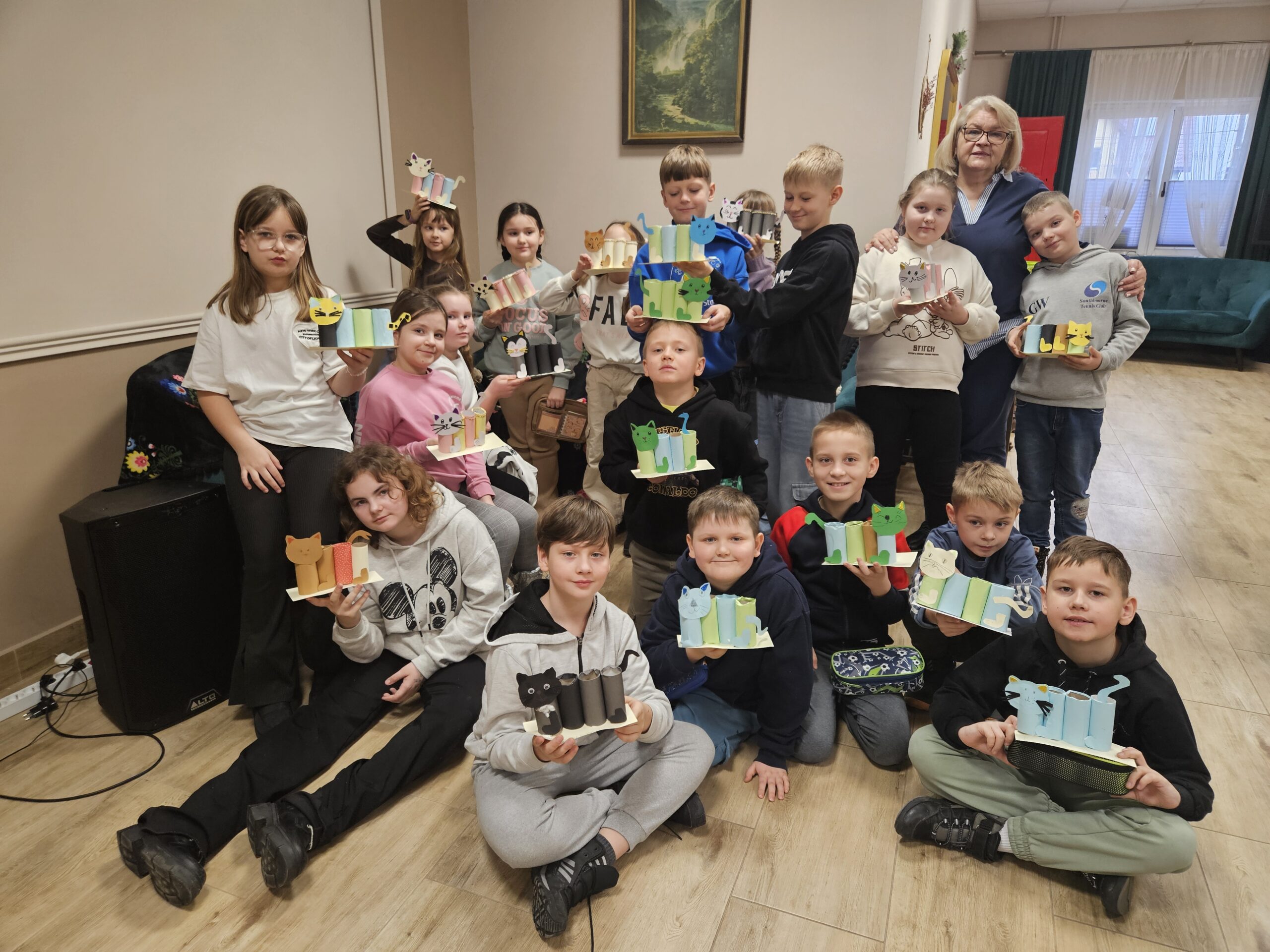 Grupowe zdjęcie dzieci trzymających w rękach przyborniki z papieru w kształcie kota oraz ich nauczycielka.