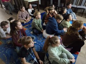20260225_083021 Dzieci siedzą na dywanie i oglądają prezentację.