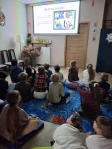 20260225_083138 Dzieci siedzą na dywanie i oglądają prezentację.