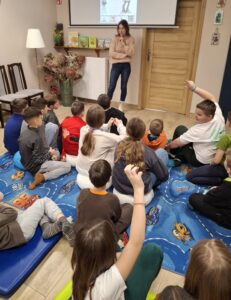 20260225_094453 Dzieci siedzą na dywanie i oglądają prezentację.