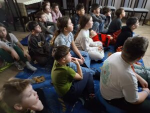 20260225_095329 Dzieci siedzą na dywanie i oglądają bajkę animowaną.