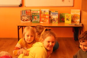 IMG_0491 Dzieci siedzą na dywanie na tle książek.