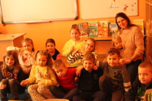 IMG_0494 Dzieci oraz prowadząca zajęcia siedzą na dywanie i oglądają bajkę animowaną.