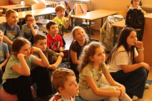 IMG_0495 Dzieci siedzą na dywanie i oglądają bajkę animowaną.