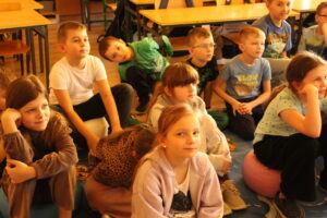 IMG_0496 Dzieci siedzą na dywanie i oglądają bajkę animowaną.