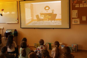 IMG_0498 Dzieci siedzą na dywanie i oglądają bajkę animowaną.