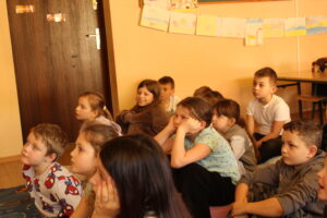 IMG_0499 Dzieci siedzą na dywanie i oglądają bajkę animowaną.