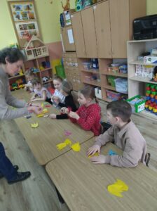 Dzieci i instruktorka podczas warsztatów robienia tulipanów z papieru.