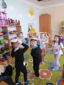 Dzieci bawiące się z książkami na głowach.