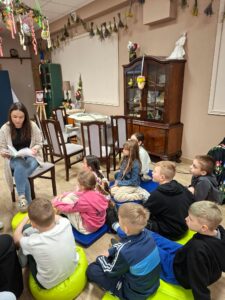 Dzieci siedzące na podłodze oraz kobieta, która czyta im książkę.