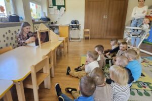 Grupa dzieci siedząca na podłodze oglądająca teatrzyk Kamishibai.