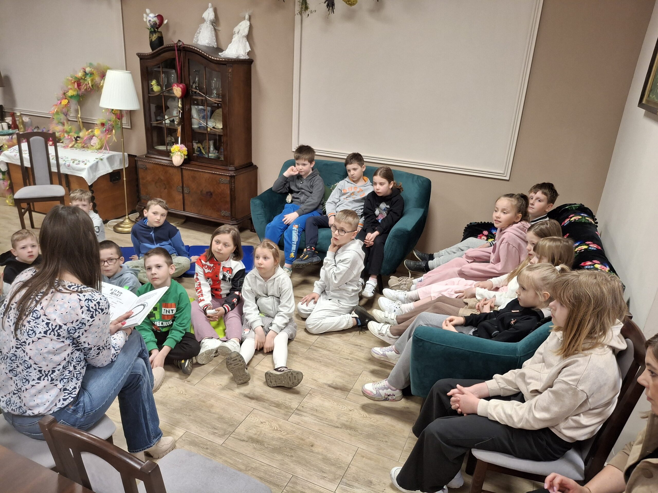 Dzieci słuchające książki czytanej przez kobietę.