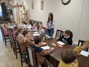 Grupa dzieci rysujących kredkami oraz kobieta.