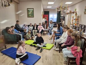 Grupa dzieci i nauczycielka słuchają czytanej książki przez kobietę.