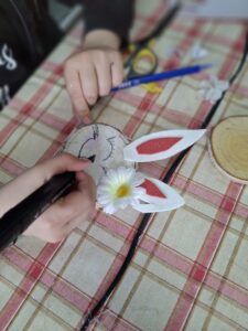 Dziecięce dłonie rysują uśmiech zajączkowi, wykonanemu z plastra drzewa.