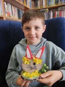 hłopiec trzymający w rękach zajączka, wykonanego własnoręcznie z plastrów drzewa i ozdób.